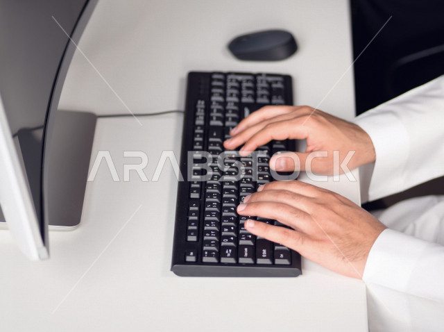 Close-up of the hand of a Saudi Arabian Gulf man working in customer service, inquiries and inquiries, answering customer questions, making video call through the computer, follow-up and development of work, data entry
