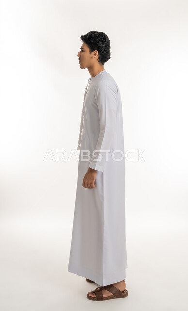 الاهتمام بالمظهر الخارجي, مفهوم الأناقة و الرجولة, بورتريه من الجانب لشاب مراهق عربي خليجي إماراتي يرتدي الكندورة يقف باستقامة و اعتدال, الجسم بالطول الكامل, خلفية بيضاء