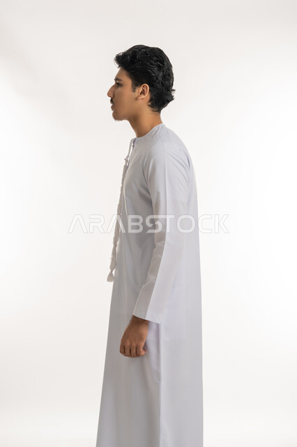 The concept of elegance and masculinity, interest in external appearance, side portrait of an Arab Gulf Emirati teenager wearing a kandura, standing straight and upright, white background