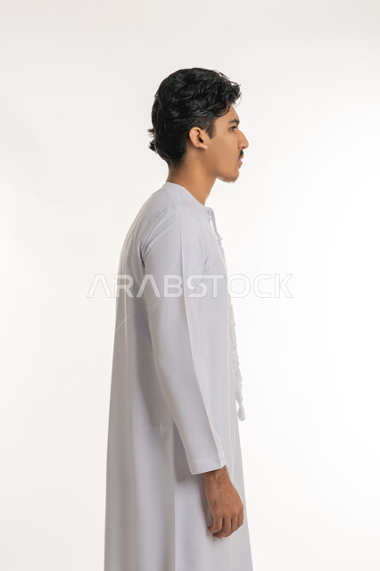 مفهوم الأناقة و الرجولة, الاهتمام بالمظهر الخارجي, بورتريه من الجانب لشاب مراهق عربي خليجي إماراتي يرتدي الكندورة يقف باستقامة و اعتدال, خلفية بيضاء