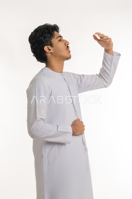 Indigestion and feeling of colic, feeling stomach pain, asking for help to go to the doctor, looking at something above, portrait of a young Arab Gulf Emirati teenager wearing a kandura putting his hand on his stomach with gestures of pain, white background