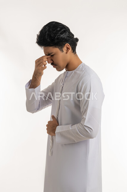 الصداع و آلام الرأس, الحاجة للفحص والعلاج، التهاب القرنية العينية, مشاكل في النظر, بورتريه لشاب مراهق عربي خليجي إماراتي يرتدي الكندورة يضع يده على وجهه بتعابير الألم, خلفية بيضاء