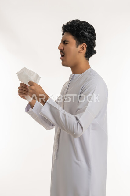 التهاب الأنف و الجيوب التحسسية, الشعور بالمرض و الزكام, الحاجة إلى العلاج والدواء, بورتريه لشاب مراهق عربي خليجي إماراتي يرتدي الكندورة يضع منديل ورقي على وجهه بإيماءات العطاس, خلفية بيضاء