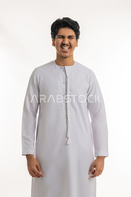 العناية والاهتمام بصحة ونظافة الفم, تجنب التسوس وأمراض اللثة, مفهوم تبييض وتجميل ومعالجة الأسنان، بورتريه لشاب مراهق عربي خليجي إماراتي يرتدي الكندورة يقف باستقامة ويظهر أسنانه, خلفية بيضاء