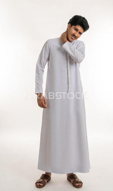 الحاجة للعلاج الفيزيائي، الإحساس بالتعب والإرهاق, وجع مفاصل و عظام الرقبة, آلام العنق والعمود الفقري, بورتريه لشاب مراهق عربي خليجي إماراتي يرتدي الكندورة يضع يده حول عنقه بإيماءات الألم, الجسم بالطول الكامل, خلفية بيضاء