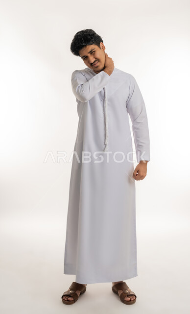 وجع مفاصل و عظام الرقبة, آلام العنق والعمود الفقري, الحاجة للعلاج الفيزيائي، الإحساس بالتعب والإرهاق, بورتريه لشاب مراهق عربي خليجي إماراتي يرتدي الكندورة يضع يده حول عنقه بإيماءات الألم, الجسم بالطول الكامل, خلفية بيضاء