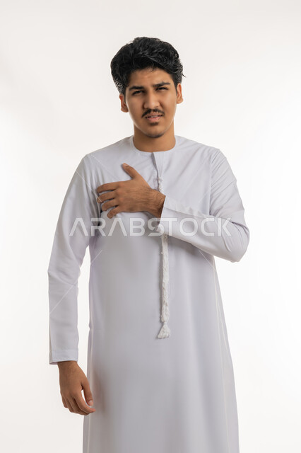 الإحساس بذبحة صدرية, التعب والإرهاق والضغوطات النفسية، اضطرابات وأمراض قلبية, الشعور في زيادة معدل ضربات القلب, بورتريه لشاب مراهق عربي خليجي إماراتي يرتدي الكندورة يضع يده على صدره بإيماءات الألم, خلفية بيضاء