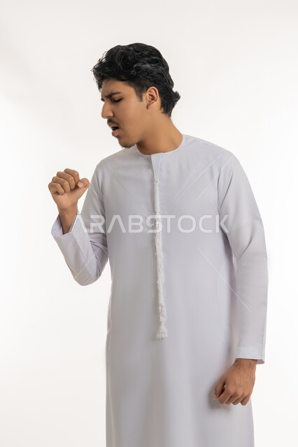 الشعور بالمرض و الكحة, الحاجة إلى زيارة الطبيب و العلاج, الإصابة بفايروس كورونا، الانفلونزا والتهاب الرئة, بورتريه لشاب مراهق عربي خليجي إماراتي يرتدي الكندورة يرفع يده إلى فمه بإيماءات السعال, خلفية بيضاء