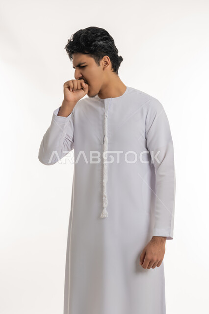 الإصابة بفايروس كورونا، الانفلونزا والتهاب الرئة, الشعور بالمرض و الكحة, الحاجة إلى زيارة الطبيب و العلاج, بورتريه لشاب مراهق عربي خليجي إماراتي يرتدي الكندورة يرفع يده إلى فمه بإيماءات السعال, خلفية بيضاء