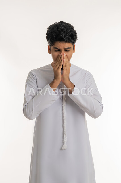 الشعور بالمرض و الزكام, الحاجة إلى العلاج والدواء, التهاب الأنف و الجيوب التحسسية, بورتريه لشاب مراهق عربي خليجي إماراتي يرتدي الكندورة يضع يديه على وجهه بإيماءات العطاس, خلفية بيضاء