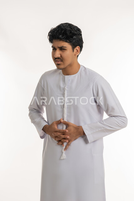 عسر الهضم والشعور بالمغص, الإحساس بآلام في المعدة, طلب المساعدة للذهاب إلى الطبيب، الحاجة للدواء ووضع خطة علاجية، بورتريه لشاب مراهق عربي خليجي إماراتي يرتدي الكندورة يضع يديه على بطنه بإيماءات الألم, خلفية بيضاء