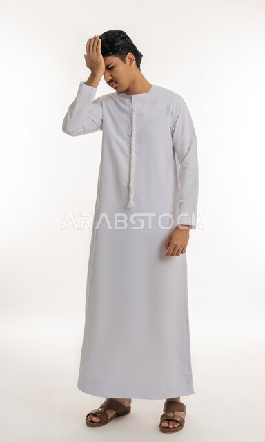 الإحساس بالدوار و وجع الرأس, الحاجة إلى العلاج و الراحة, الشعور بالمرض و التعب, آلام الشقيقة والصداع النصفي, بورتريه لشاب مراهق عربي خليجي إماراتي يرتدي الكندورة يضع يده على رأسه بإيماءات الانزعاج و الألم, الجسم بالطول الكامل, خلفية بيضاء