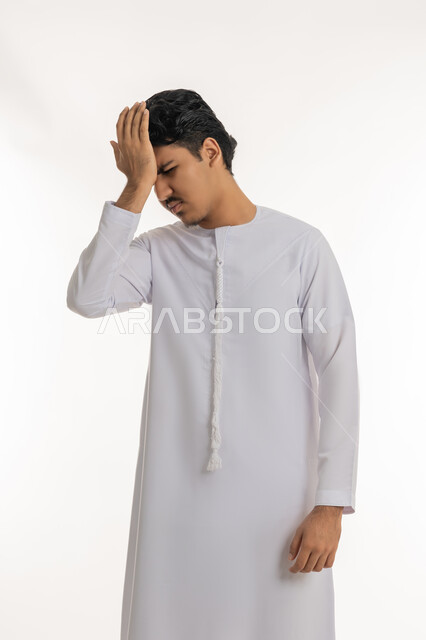 آلام الشقيقة والصداع النصفي, الإحساس بالدوار و وجع الرأس, الحاجة إلى العلاج و الراحة, الشعور بالمرض و التعب, بورتريه لشاب مراهق عربي خليجي إماراتي يرتدي الكندورة يضع يده على رأسه بإيماءات الانزعاج و الألم, خلفية بيضاء