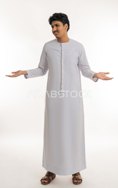 تعابير الاستفهام و عدم الفهم و الحيرة, الاستفسار و التساؤل عن شيء معين, بورتريه لشاب مراهق عربي خليجي إماراتي يرتدي الكندورة يشير بيديه بإيماءات الاستغراب و التعجب, الجسم بالطول الكامل, خلفية بيضاء