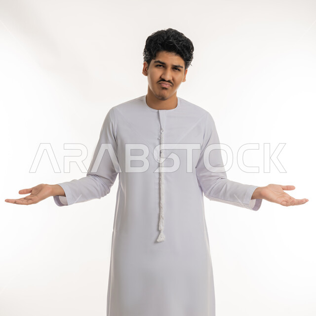 تعابير عدم الفهم و الحيرة و الاستفهام, الاستفسار و التساؤل عن شيء معين, بورتريه لشاب مراهق عربي خليجي إماراتي يرتدي الكندورة يشير بيديه بإيماءات الاستغراب و التعجب, خلفية بيضاء