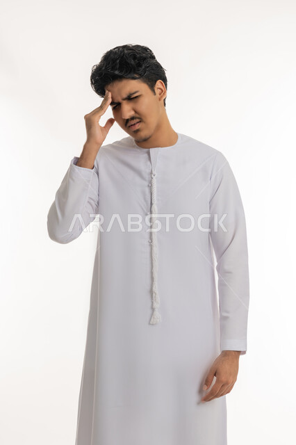 آلام الشقيقة والصداع النصفي, الإحساس بالدوار و وجع الرأس, الحاجة إلى العلاج و الراحة, الشعور بالمرض و  التعب, بورتريه لشاب مراهق عربي خليجي إماراتي يرتدي الكندورة يضع يده على رأسه بإيماءات الانزعاج و الألم, خلفية بيضاء