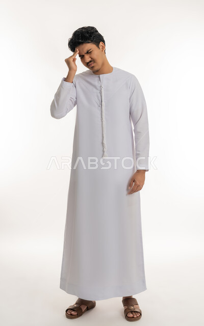 الإحساس بالدوار و وجع الرأس, الحاجة إلى العلاج و الراحة, الشعور بالمرض و  التعب, آلام الشقيقة والصداع النصفي, بورتريه لشاب مراهق عربي خليجي إماراتي يرتدي الكندورة يضع يده على رأسه بإيماءات الانزعاج و الألم, الجسم بالطول الكامل, خلفية بيضاء