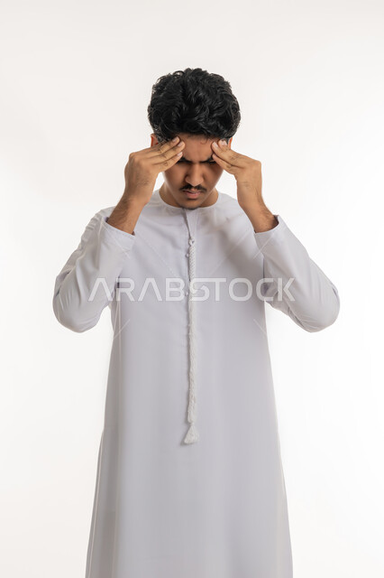 الشعور بالمرض و  التعب, آلام الشقيقة والصداع النصفي, الإحساس بالدوار و وجع الرأس, الحاجة إلى العلاج و الراحة, بورتريه لشاب مراهق عربي خليجي إماراتي يرتدي الكندورة يضع يديه على رأسه بإيماءات الانزعاج و الألم, خلفية بيضاء