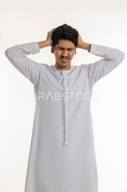 الشعور بالمرض و  التعب, آلام الشقيقة والصداع النصفي, الإحساس بالدوار و وجع الرأس, الحاجة إلى العلاج و الراحة, بورتريه لشاب مراهق عربي خليجي إماراتي يرتدي الكندورة يضع يديه على رأسه بإيماءات الانزعاج و الألم, خلفية بيضاء