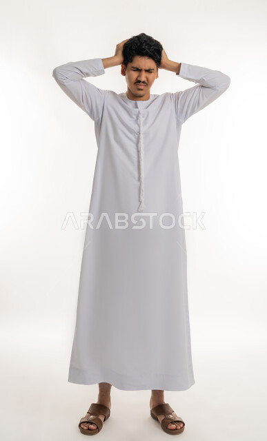 الحاجة إلى العلاج و الراحة, الشعور بالمرض و  التعب, آلام الشقيقة والصداع النصفي, الإحساس بالدورا و وجع الرأس, بورتريه لشاب مراهق عربي خليجي إماراتي يرتدي الكندورة يضع يديه على رأسه بإيماءات الانزعاج و الألم, الجسم بالطول الكامل, خلفية بيضاء