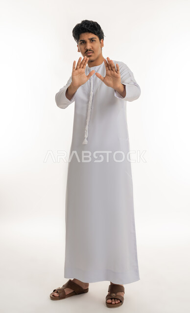 Stop, Refrain and Do Not Approach Request, Protecting Oneself from External Harm, Portrait of a Young Arab Emirati Gulf Teenager Wearing a Kandora Looking at the Camera and Raising His Hands with Expressions of Fear and Away, Full Length Body, White Background