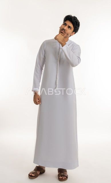 شرود الذهن والتأمل والتخطيط للمستقبل، التفكير لإيجاد حل مشكلة ما، مواجهة المشكلات والتحديات, بورتريه لشاب مراهق عربي خليجي إماراتي يرتدي الكندورة ينظر إلى الأعلى و يضع يده على ذقنه بتعابير التركيز و التمعن, الجسم بالطول الكامل, خلفية بيضاء