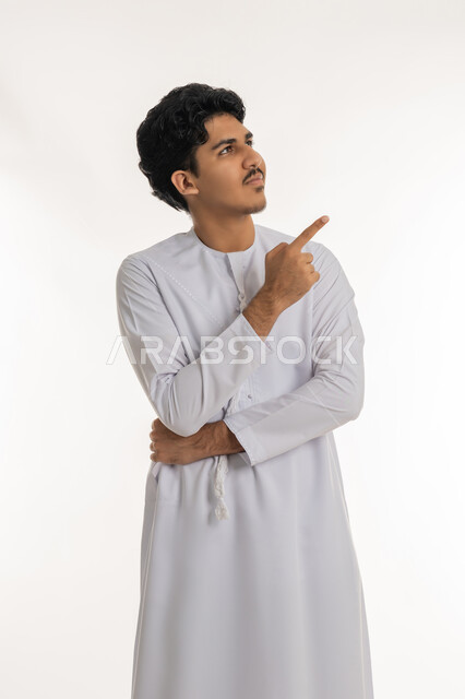 Pointing and explaining something, specifying a specific location, indicating the location of an item, portrait of a young Emirati Gulf Arab teenager wearing a kandura looking up and pointing with his index finger at something, white background