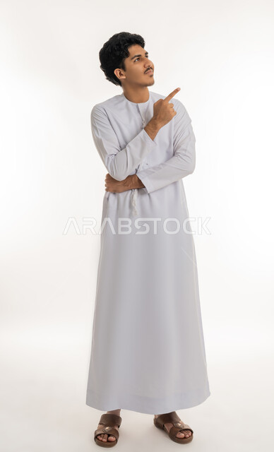 تحديد موقع معين, الإشارة و التوضيح إلى شيء ما, الدلالة على مكان عنصر، بورتريه لشاب مراهق عربي خليجي إماراتي يرتدي الكندورة ينظر إلى الأعلى و يشير بإصبع السبابة إلى شيء ما, الجسم بالطول الكامل، خلفية بيضاء