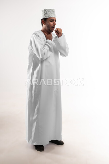 الانفلونزا والتهاب الرئة، الشعور بالمرض والكحة، الحاجة الى العلاج والدواء, بورتريه لشاب عربي خليجي عماني يرتدي الدشداشة و الكمه يضع يديه على رقبته بإيماءات ضيق التنفس, الشعور بالاختناق والتعب الشديد، صورة الجسم بالطول الكامل, خلفية بيضاء