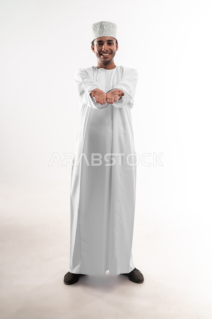 رفع وحمل العناصر، استخدام حاسة اللمس لتحريك العناصر الهولوجراميه، بورتريه لشاب عربي خليجي عماني يرتدي الدشداشة ينظر الى الكاميرا يحمل شئ بين يديه، تقديم وعرض عنصر ما، صورة الجسم بالطول الكامل، خلفية بيضاء