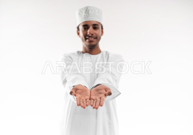 رفع وحمل العناصر، استخدام حاسة اللمس لتحريك العناصر الهولوجراميه، بورتريه مقرب لشاب عربي خليجي عماني يرتدي الدشداشة ينظر الى الكاميرا يحمل شئ بين يديه، تقديم وعرض عنصر ما، خلفية بيضاء