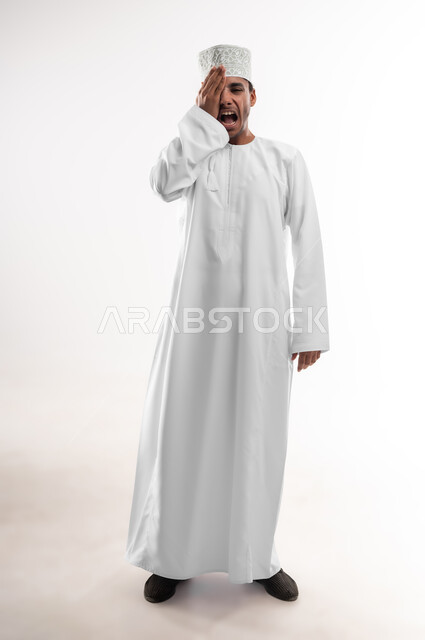 عدم القدرة على فتح العينين، مشاكل عينيه وحالات مرضية، الحاجة للفحص والعلاج، التهاب القرنية العينية، بورتريه لشاب عربي خليجي عماني يرتدي الدشداشة والكمه يضع يده على عينه بإيماءات الألم, صورة الجسم بالطول الكامل, خلفية بيضاء
