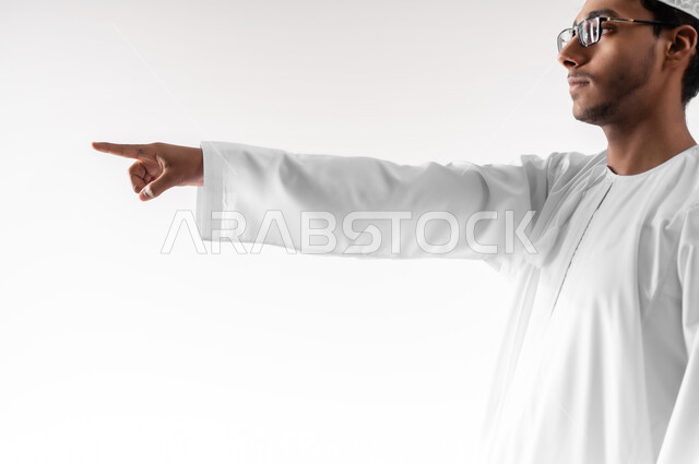 تحديد موقع معين، بورتريه مقرب لشاب عربي خليجي عماني يرتدي الدشداشة والكمه والنظارات الطبية يرفع يده للاعلى يشير بأصبع السبابة الى هدف محدد، مفهوم النقر والضغط والتفاعل مع العناصر الهولوجرامية، خلفية بيضاء