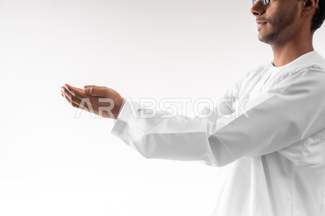 الاجتهاد في العبادة والتقرب إلى رب العالمين، بورتريه مقرب لشاب عربي خليجي عماني يرتدي الدشداشة و الكمه يرفع يديه ويدعو الله بإيماءات التوسل والتضرع، الرغبة في تحقيق الأمنيات، خلفية بيضاء