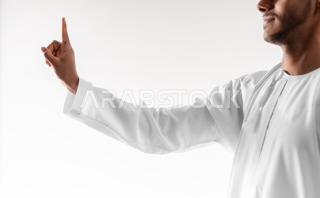 تعابير تدل على الرقم واحد, بورتريه مقرب لشاب عربي خليجي عماني يرتدي الدشداشة و الكمه مبتسم يرفع اصبع السبابة الى الاعلى بإيماءات التحذير والتنبيه، خلفية بيضاء
