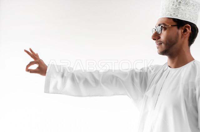 علامة الجوده و الإمتياز والتميز, مفهوم القبول والموافقه، بورتريه مقرب لشاب عربي خليجي عماني مبتسم يرتدي الدشداشة والكمه والنظارات الطبية يرفع يديه للاعلى بإيماءات الإعجاب والرضا، خلفية بيضاء