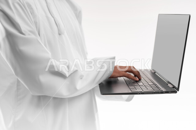 إستخدام الأجهزة التقنية الحديثة، مفهوم التطور والتقدم التكنولوجي، بورتريه مقرب لشاب عربي خليجي عماني يرتدي الدشداشة يقوم باستخدام الحاسب المحمول، إنجاز مهام العمل عن بعد عبر اللابتوب، خلفية بيضاء