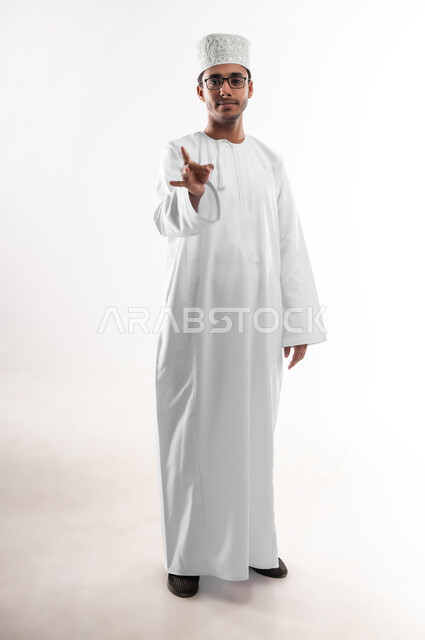 التواصل مع ذوي الهمم سمعيا أو صوتيا، تعليم لغات الإشارة للصم والبكم، الاهتمام بالأناقة والمظهر الخارجي، بورتريه لشاب عربي خليجي عماني يرتدي الدشداشة والكمه والنظارة الطبية ينظر الى الكاميرا يرفع يده بدلالة الرقم ثمانية، صورة الجسم بالطول الكامل، خلفية بيضاء