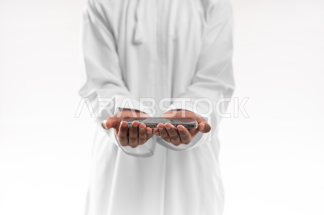 Using advanced technology, displaying mobile applications and services, close-up portrait of a young Omani Gulf Arab man wearing a dishdasha holding a mobile phone with a blank black screen, e-shopping concept, white background