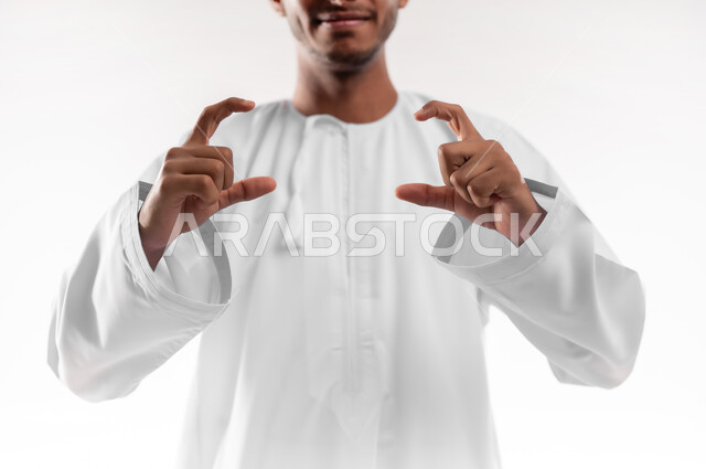 تقدير وقياس حجم الأشياء، مفهوم تقديم وعرض عنصر معين، بورتريه لشاب عربي خليجي عماني يرتدي الدشداشة يرفع يديه للاعلى يمسك عنصر هولوجرامي، محاولة التقاط الصور، خلفية بيضاء