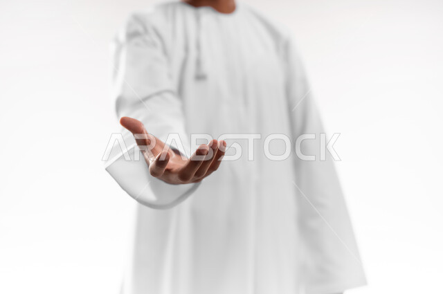 إمساك و إحتواء عنصر ما، مفهوم الاناقة و الاهتمام بالمظهر الخارجي, بورتريه مقرب لشاب عربي خليجي عماني يرتدي الدشداشة يمد يده للأمام يحاول التقاط عناصر هولوجرامية ثلاثية الأبعاد، خلفية بيضاء