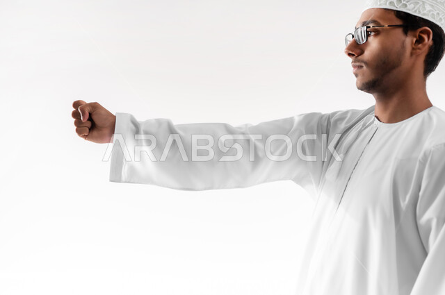 الترحيب و السلام و إلقاء التحية، بناء علاقات و تكوين صداقات جديدة، بورتريه مقرب لشاب عربي خليجي عماني يرتدي الدشداشة والكمه والنظارة الطبية يقوم بتوجيه قبضة يده بإيماءات القوة والإصرار والمواجهة، خلفية بيضاء