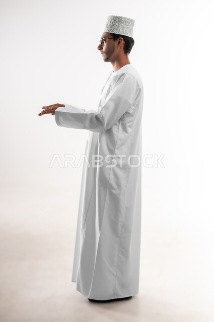 استخدام حاسة اللمس لتحريك العناصر الهولوجراميه، بورتريه لشاب عربي خليجي عماني يرتدي الدشداشة والكمه والنظارة الطبية يمد يديه للأمام بإيماءات العزف على آلة البيانو، حركات يدين مختلفة، صورة الجسم بالطول الكامل، خلفية بيضاء