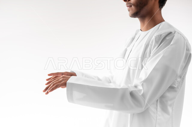 استخدام حاسة اللمس لتحريك العناصر الهولوجراميه، بورتريه لشاب عربي خليجي عماني يرتدي الدشداشة يمد يديه للأمام بإيماءات العزف على آلة البيانو، حركات يدين مختلفة، خلفية بيضاء