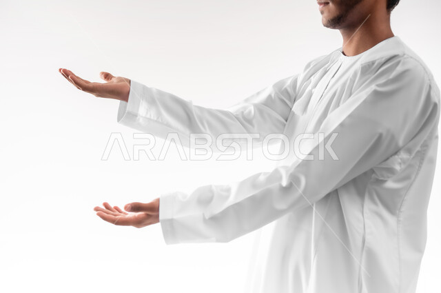 رفع وحمل شيء ما، استخدام حاسة اللمس لتحريك العناصر الهولوجراميه، بورتريه مقرب لشاب عربي خليجي عماني يرتدي الدشداشة يرفع يده للاعلى بإيماءات الموازنة وتقدير الحجم، خلفية بيضاء