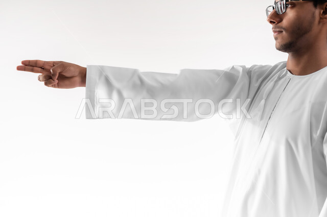 مفهوم الاختيار و تحديد موقع معين، بورتريه مقرب لشاب عربي خليجي عماني يرتدي الدشداشة والنظارات الطبية يرفع يده للاعلى يشير الى هدف محدد، حركات يدين تدل على التحذير والتنبيه، خلفية بيضاء