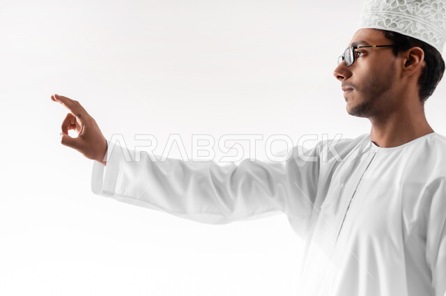 التفاعل مع العناصر الهولوجرامية، مفهوم الاختيار و تحديد موقع معين، بورتريه مقرب لشاب عربي خليجي عماني يرتدي الدشداشة والكمه والنظارات الطبية يرفع يده للاعلى يشير الى هدف محدد، خلفية بيضاء