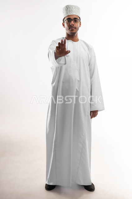 Holding and containing an element, the concept of elegance and interest in the external appearance, a portrait of a young Arab Gulf Omani man wearing a dishdasha, a sleeve and medical glasses, looking at the camera, extending his hand forward, trying to capture three-dimensional holographic elements, a full-length body image, white background