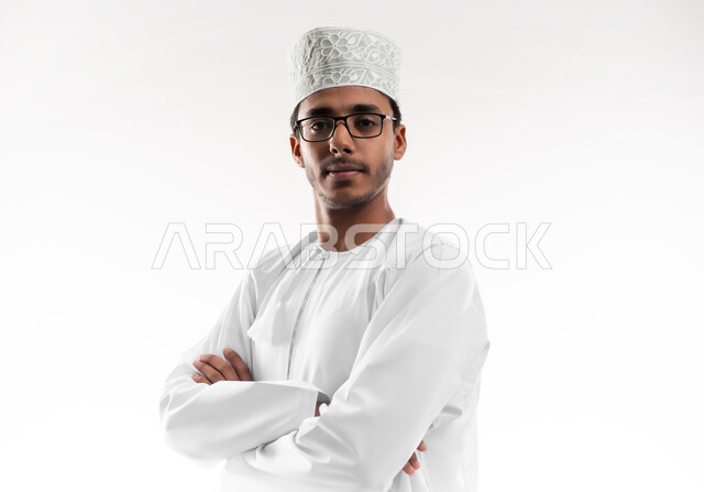 Expressions of masculinity and self-confidence, the concept of elegance and interest in external appearance, a close-up portrait of a young Gulf Arab Omani man wearing a dishdasha, a cufflink and eyeglasses, looking at the camera with gestures of happiness and pleasure, white background