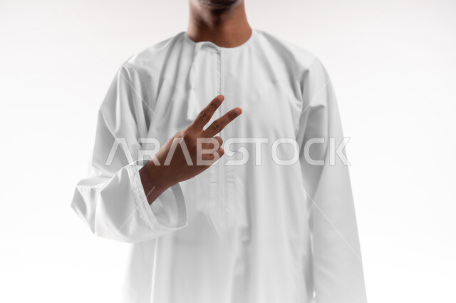 Success and achieving goals, concept of happiness in reaching goals, close-up portrait of a young Gulf Arab Omani man wearing a dishdasha raising his hand in a victory and strength sign, concept of winning and triumph, white background